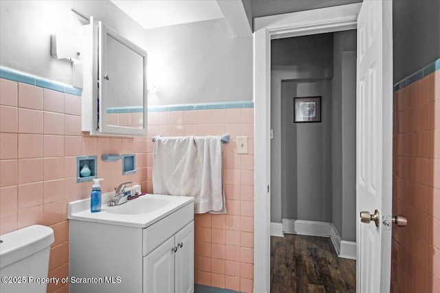 bathroom with wood finished floors, vanity, toilet, and tile walls