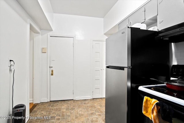 kitchen with white cabinets, decorative backsplash, stove, freestanding refrigerator, and stone finish flooring