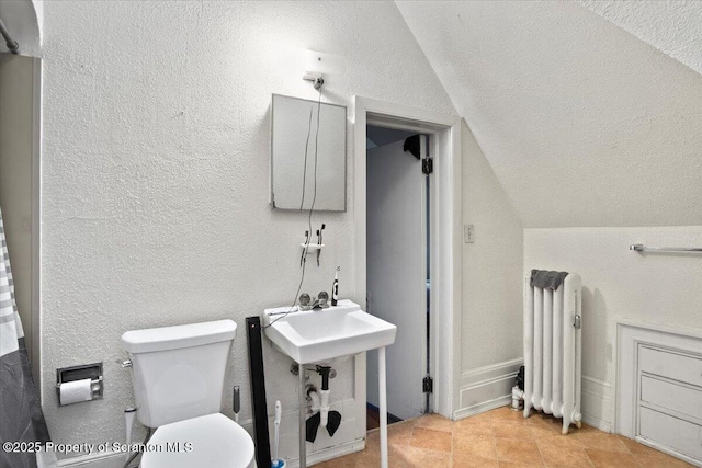 bathroom with toilet, radiator heating unit, vaulted ceiling, and a textured wall