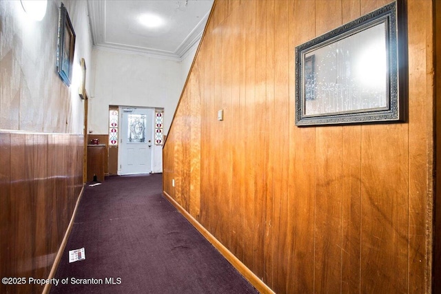 corridor featuring wood walls, dark carpet, and crown molding