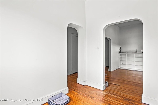 spare room featuring baseboards, arched walkways, and wood finished floors