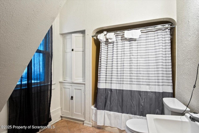 full bathroom featuring a textured wall, a shower with shower curtain, toilet, a sink, and tile patterned flooring