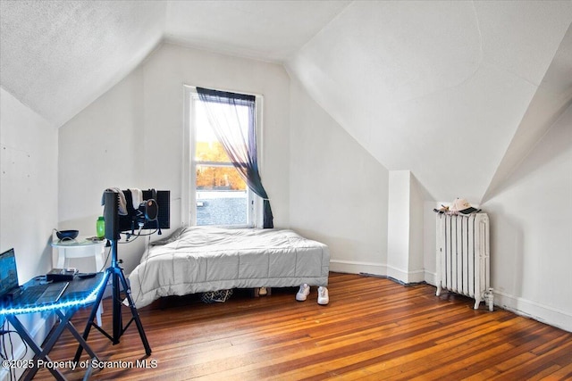 bedroom with a textured ceiling, baseboards, vaulted ceiling, radiator, and hardwood / wood-style floors