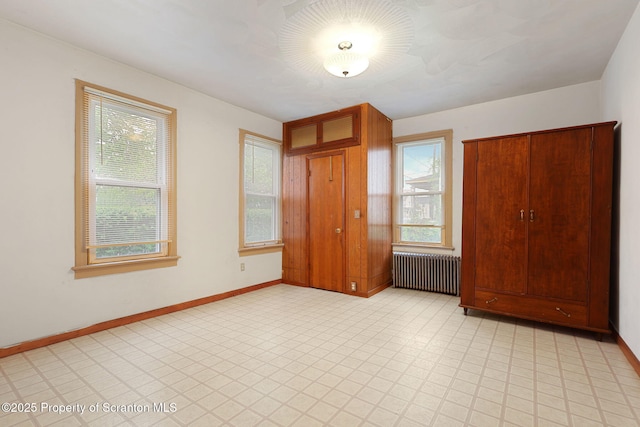 unfurnished bedroom with radiator heating unit, multiple windows, baseboards, and light flooring