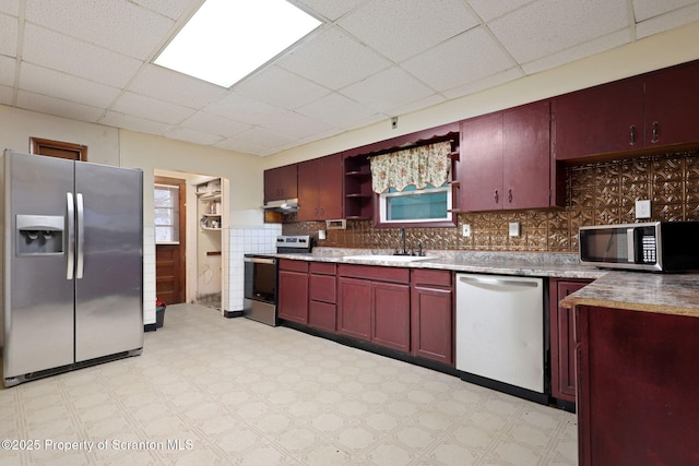 kitchen with appliances with stainless steel finishes, a sink, light flooring, under cabinet range hood, and a drop ceiling