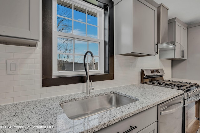 kitchen with gray cabinetry, sink, light stone countertops, tasteful backsplash, and stainless steel appliances