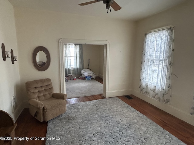 living area featuring a ceiling fan, baseboards, and wood finished floors