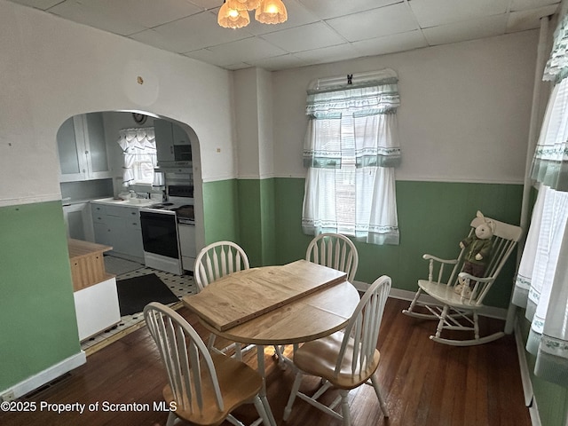 dining room with dark wood-style floors, baseboards, arched walkways, and a drop ceiling