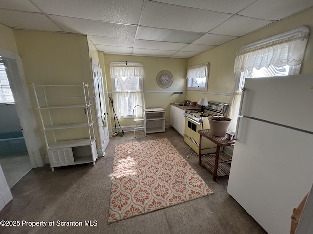 kitchen featuring white appliances, a drop ceiling, and a sink