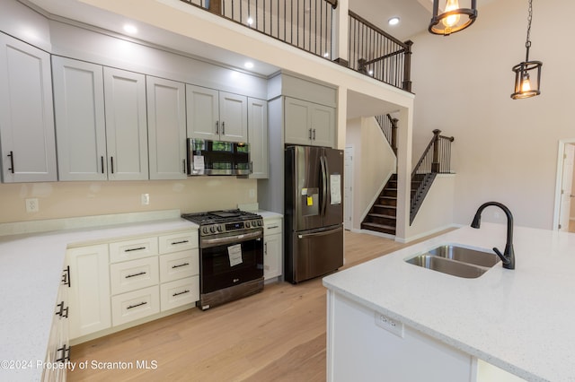 kitchen featuring appliances with stainless steel finishes, light wood-type flooring, light stone counters, sink, and pendant lighting