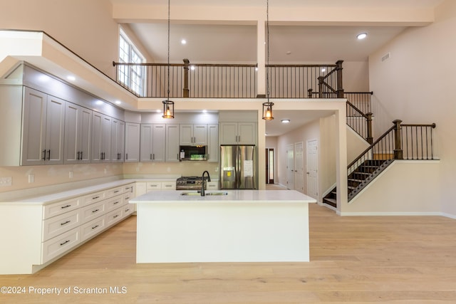 kitchen with appliances with stainless steel finishes, sink, a center island with sink, a high ceiling, and hanging light fixtures