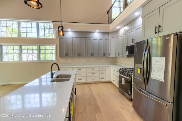 kitchen with black appliances, sink, hanging light fixtures, light wood-type flooring, and light stone counters