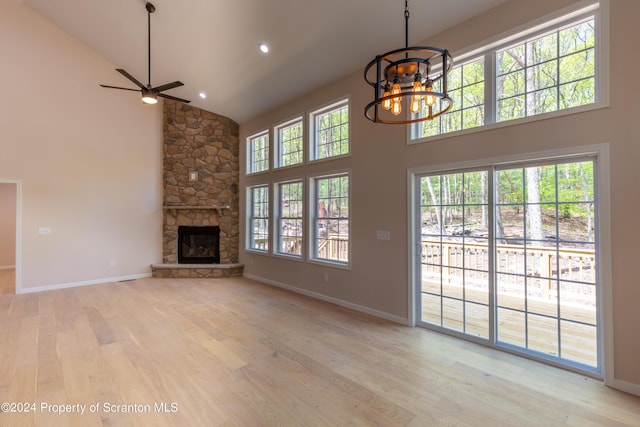 unfurnished living room with ceiling fan with notable chandelier, light wood-type flooring, a fireplace, and high vaulted ceiling