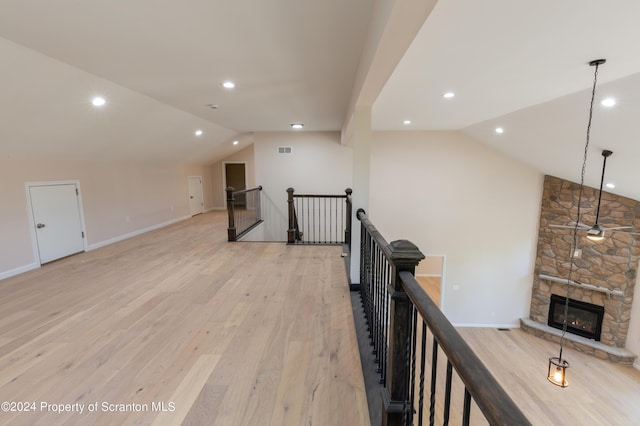 additional living space featuring a stone fireplace, lofted ceiling, and light hardwood / wood-style flooring