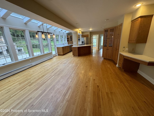 kitchen with a skylight, baseboard heating, stainless steel fridge with ice dispenser, light hardwood / wood-style flooring, and a kitchen island