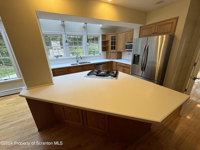 kitchen featuring kitchen peninsula, appliances with stainless steel finishes, light wood-type flooring, a kitchen bar, and sink