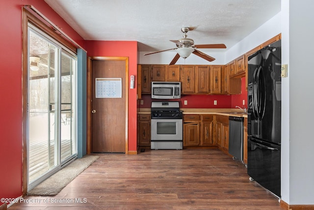 kitchen featuring a sink, light countertops, appliances with stainless steel finishes, brown cabinetry, and dark wood finished floors