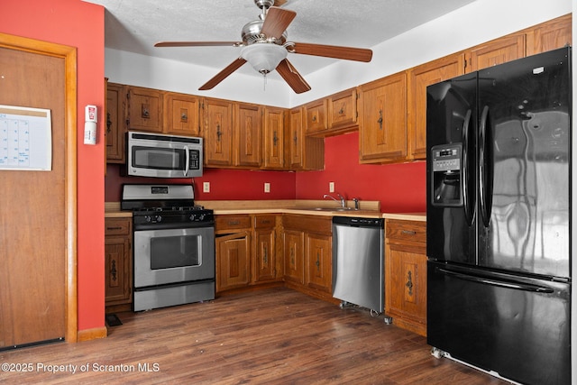 kitchen featuring light countertops, appliances with stainless steel finishes, brown cabinetry, and dark wood-type flooring