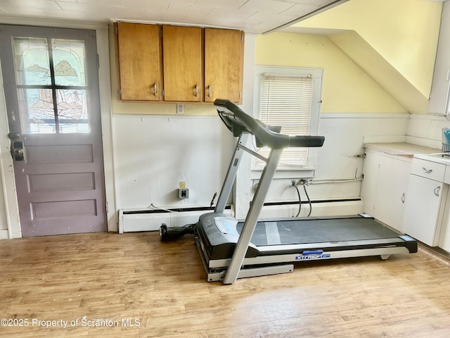 workout area with light wood-style flooring, plenty of natural light, a baseboard heating unit, and wainscoting