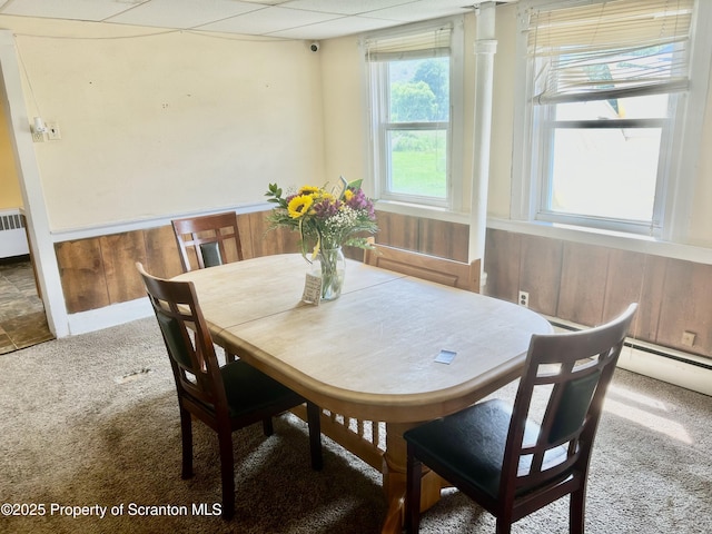 carpeted dining area featuring wood walls, a wainscoted wall, radiator heating unit, and a baseboard radiator