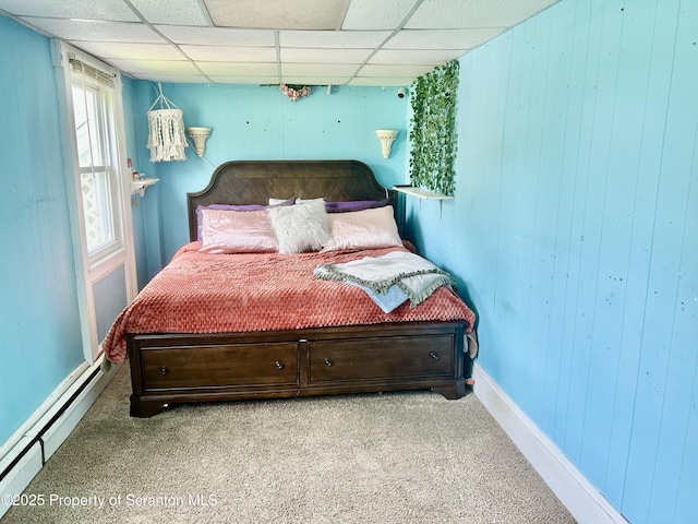 bedroom with a baseboard radiator, wood walls, carpet, and a drop ceiling
