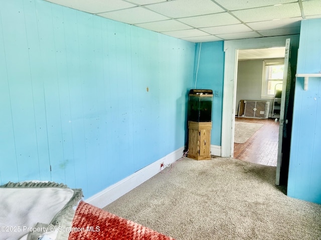 spare room featuring carpet floors, wood walls, and a drop ceiling