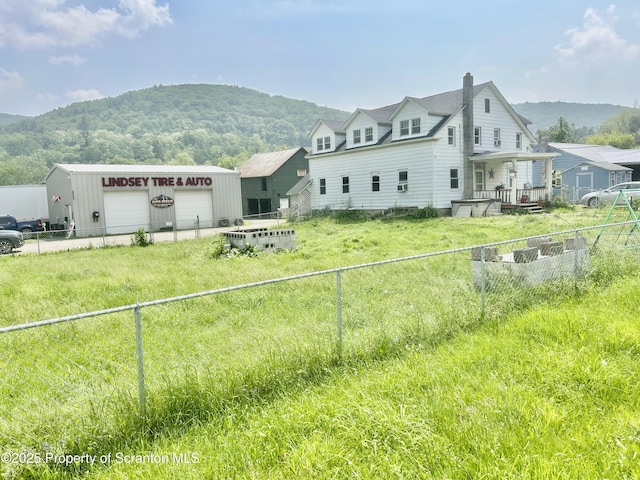 rear view of property featuring a garage, a chimney, a mountain view, and an outbuilding