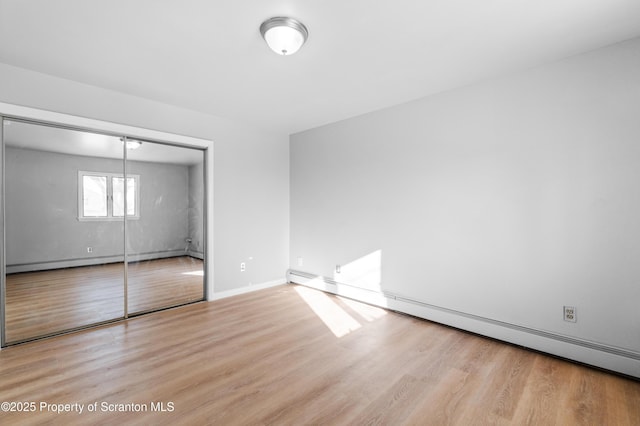 unfurnished bedroom with light hardwood / wood-style floors, a closet, and a baseboard heating unit