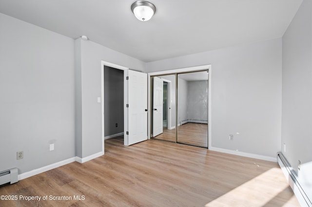 unfurnished bedroom featuring a baseboard heating unit, a closet, and light hardwood / wood-style flooring