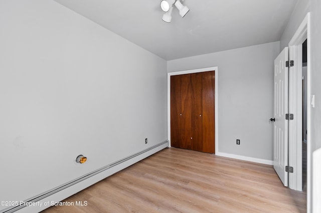 unfurnished bedroom featuring baseboard heating, a closet, and light hardwood / wood-style flooring