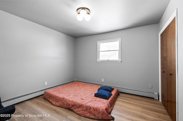 bedroom featuring a closet, light hardwood / wood-style flooring, and a baseboard heating unit