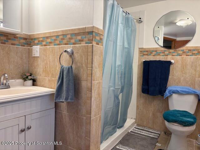 bathroom with a stall shower, toilet, a wainscoted wall, vanity, and tile walls