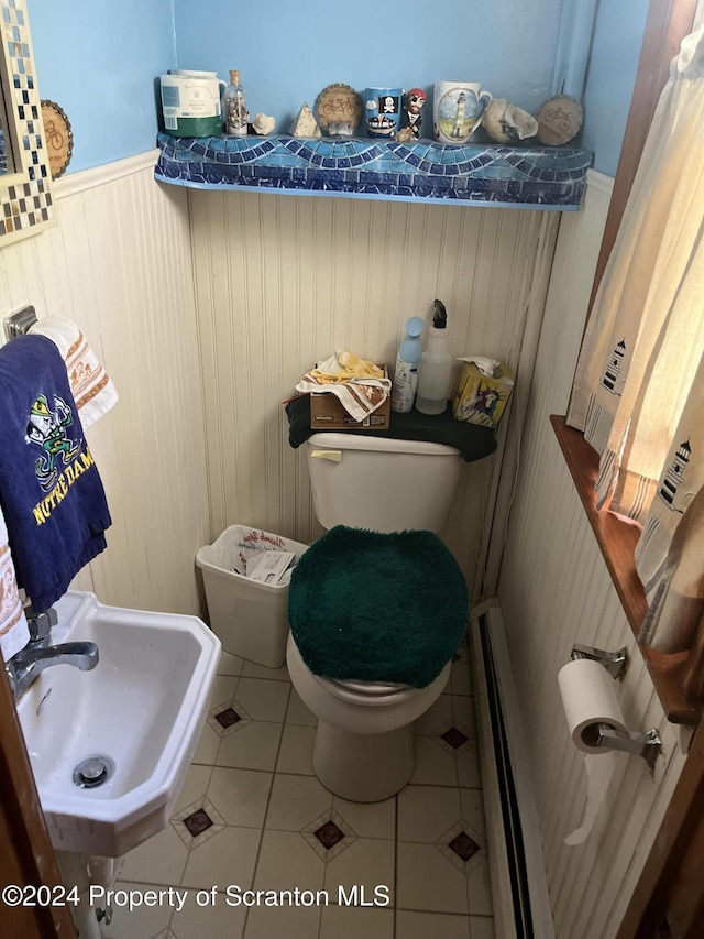 bathroom with sink, baseboard heating, tile patterned floors, wood walls, and toilet