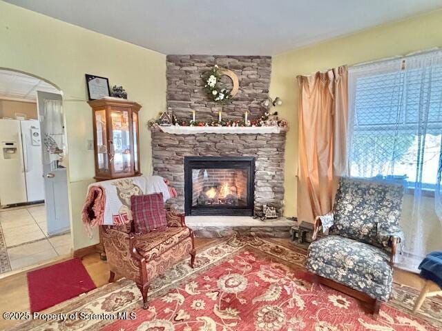 sitting room featuring arched walkways, a stone fireplace, and light tile patterned floors