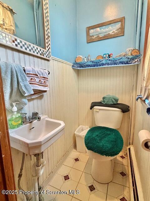 half bath with a wainscoted wall, toilet, a sink, wooden walls, and tile patterned flooring