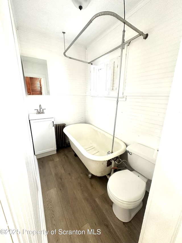 bathroom featuring toilet, radiator heating unit, a freestanding tub, wood finished floors, and vanity