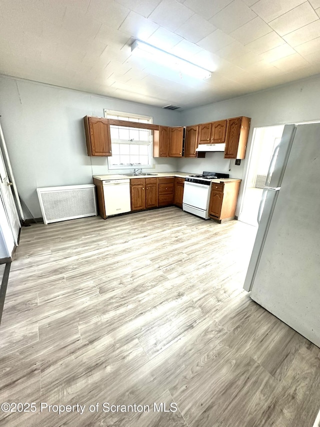 kitchen featuring light countertops, light wood-type flooring, brown cabinetry, white appliances, and a sink