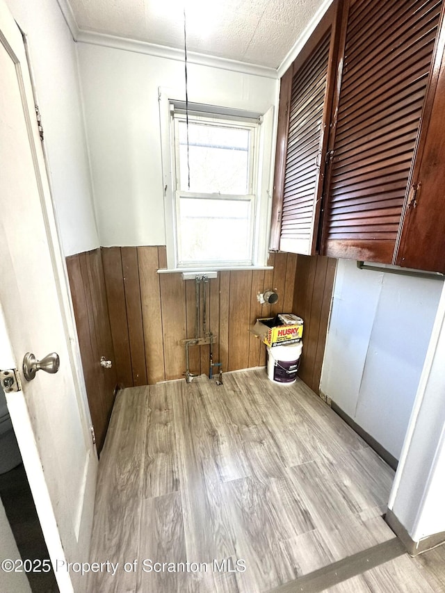 interior space featuring a wainscoted wall, a textured ceiling, crown molding, and wooden walls