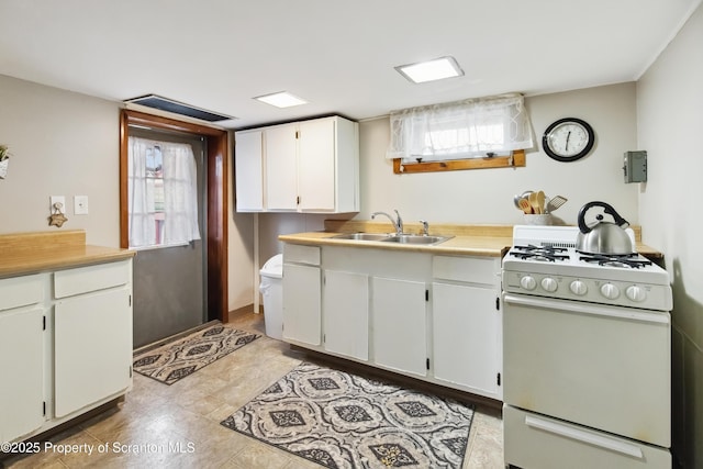 kitchen featuring white gas range oven, white cabinetry, and sink