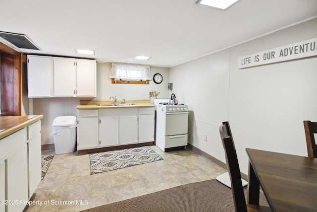 kitchen featuring white gas stove, sink, and white cabinetry