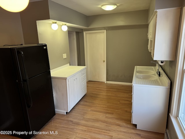 kitchen with black refrigerator, sink, light hardwood / wood-style flooring, and white cabinets