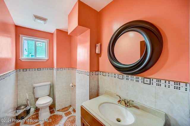 bathroom featuring tile patterned floors, vanity, toilet, and tile walls