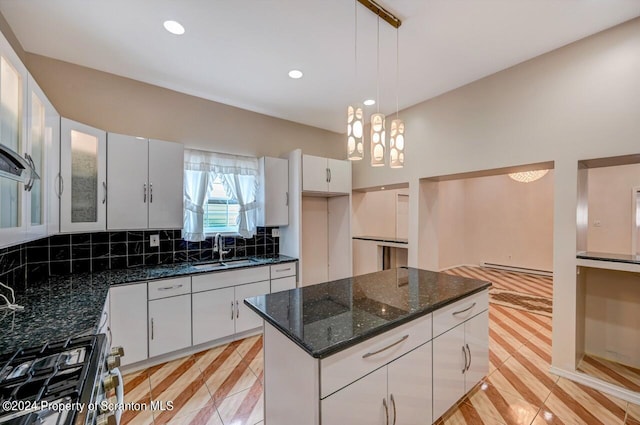 kitchen featuring pendant lighting, backsplash, dark stone counters, white cabinets, and sink