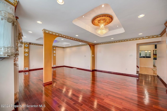 empty room with a chandelier, hardwood / wood-style flooring, and a raised ceiling