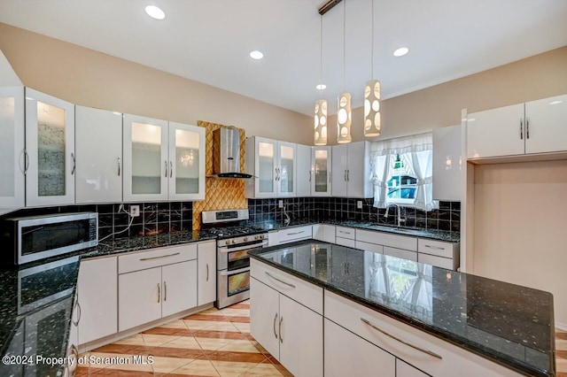 kitchen with wall chimney range hood, dark stone countertops, appliances with stainless steel finishes, decorative light fixtures, and white cabinetry