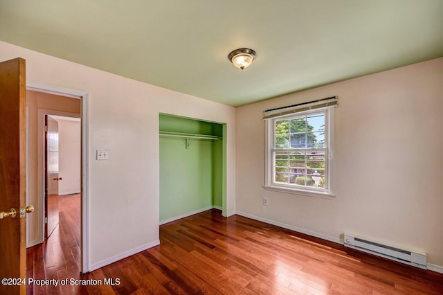 unfurnished bedroom featuring hardwood / wood-style floors, a closet, and a baseboard heating unit