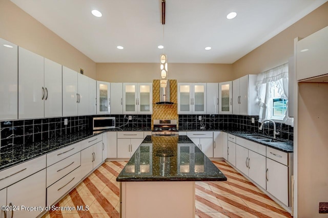 kitchen with white cabinetry, sink, wall chimney range hood, a kitchen island, and appliances with stainless steel finishes