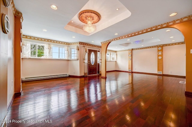 spare room with baseboard heating, a raised ceiling, a notable chandelier, and hardwood / wood-style flooring