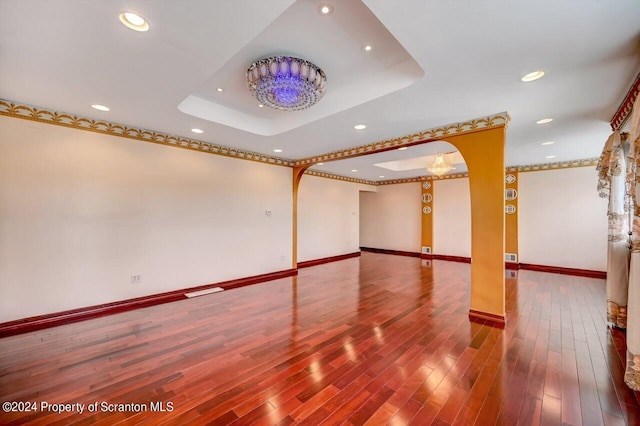 empty room featuring hardwood / wood-style flooring, a raised ceiling, and an inviting chandelier