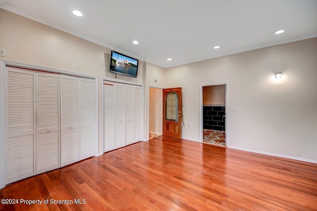 unfurnished bedroom with ornamental molding, light wood-type flooring, and multiple closets